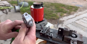 Hands holding a small cast metal part beside a mold fixture and red electric melting furnace